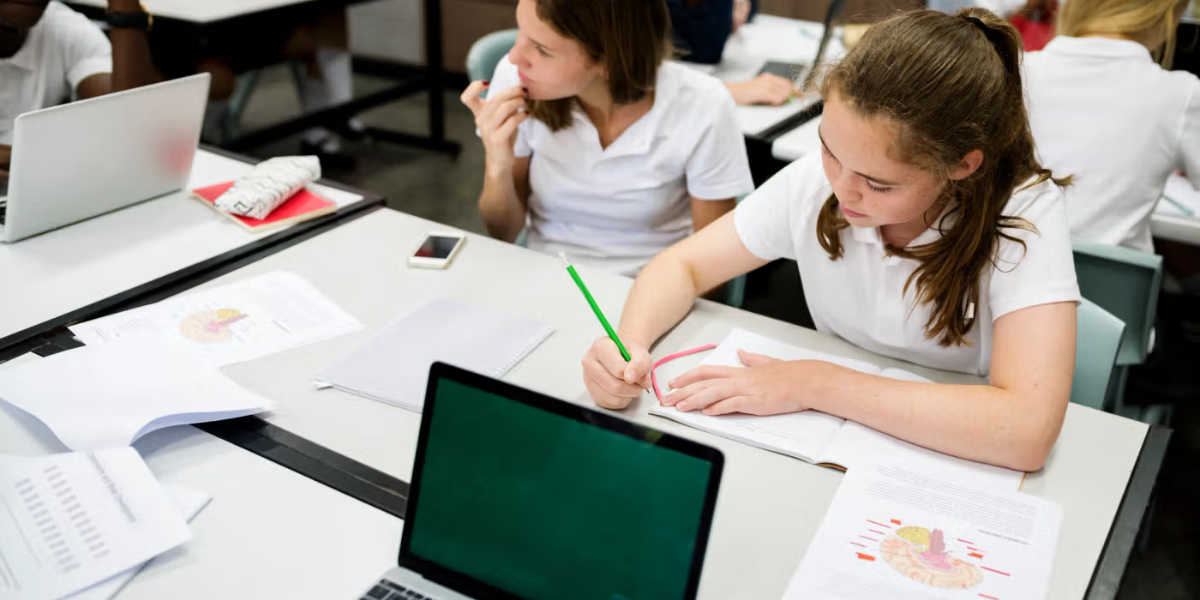Pupils working with laptops and notes in class, highlighting the value of a student information system for schools.