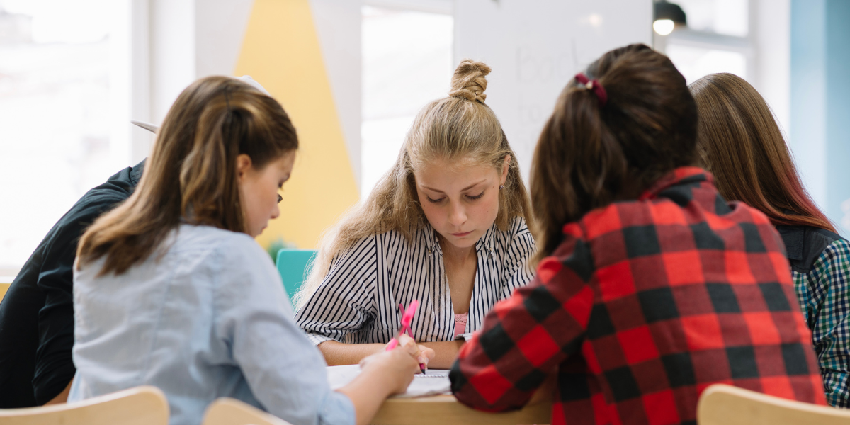 teenage girls sitting by rounded table to get stronger teamwork skills